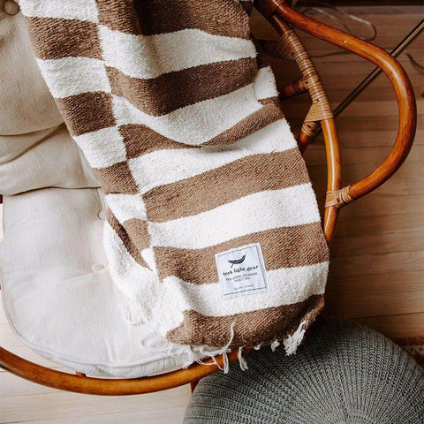 Trek Light Ocelot Blanket draped over a cozy chair, showcasing brown and white stripes, inspired by Salvador Dali's pet ocelot.