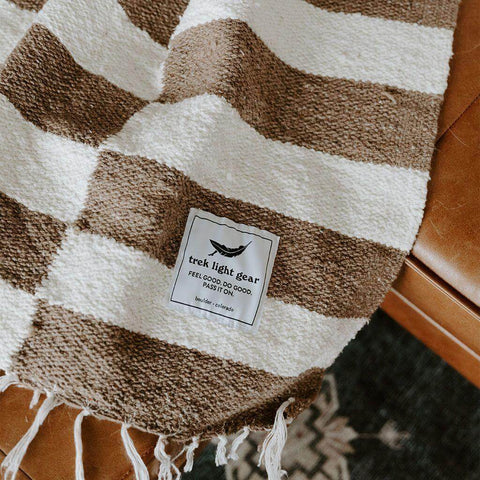 Cozy Trek Light striped blanket draped on a chair, inspired by Salvador Dali's ocelot tribute. Perfect for comfort at home or on the go.