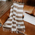 Cozy Trek Light ocelot blanket with brown and white stripes, draped over a leather couch for a stylish and warm living room accent.