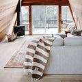 Cozy living room with a stylish Trek Light ocelot blanket draped over a sofa, showcasing warm wooden interiors and a scenic view.