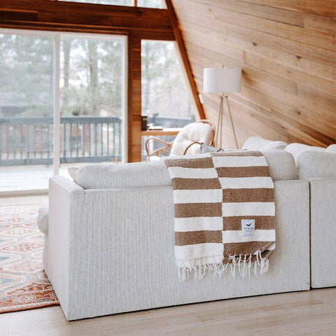 Cozy living room featuring a Trek Light Ocelot Blanket draped over a sofa with a scenic outdoor view in the background.