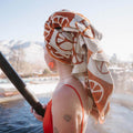 Person enjoying spa with Peace Bath Towel in vibrant design wrapped around hair, soaking up sun and snowy mountain view. Trek Light Gear.