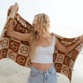 Woman enjoying beach vibes with Trek Light blanket featuring peace sign pattern