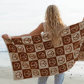 Person holding a Trek Light peace-sign patterned blanket on a beach, ocean in the background.