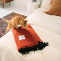Cozy Red Rocks blanket made from recycled clothing materials, handwoven, lying on bed with cat. Versatile accessory by Trek Light.