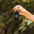 Hand holding a 'Stop. Hammock Time.' key tag outdoors, perfect for a chill day. Trek Light lifestyle accessory.
