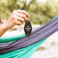 Hand holding a black "Stop. Hammock Time." key tag with green hammock in background. Perfect for a relaxing lifestyle. Trek Light.