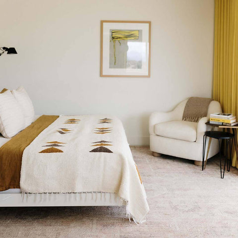 Beautiful handwoven Summit Blanket on a bed, made from recycled clothing materials, adding a cozy and versatile touch to the room decor. By Trek Light.