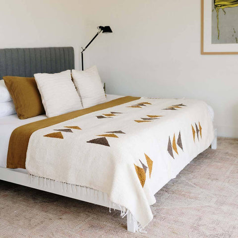 Cozy Summit Blanket made from recycled materials, showcasing handwoven design with geometric patterns on a bed. By Trek Light.