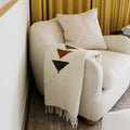 Handwoven Summit Blanket made from recycled materials draped over a cozy chair, showcasing its beautiful and versatile design. By Trek Light.