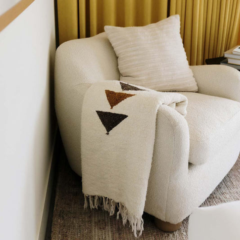 Handwoven Summit Blanket made from recycled materials draped over a cozy chair, showcasing its beautiful and versatile design. By Trek Light.