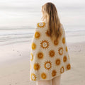 Person wrapped in sunny patterned blanket by the beach, enjoying warm comfort and tranquility.