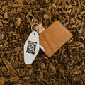 Retro-style key tag "This Must Be The Place" on wood chips, perfect for travel and adventure enthusiasts. Trek Light lifestyle accessory.