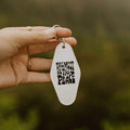 Hand holding retro 'This Must Be The Place' key tag by Trek Light, symbolizing home and adventure.