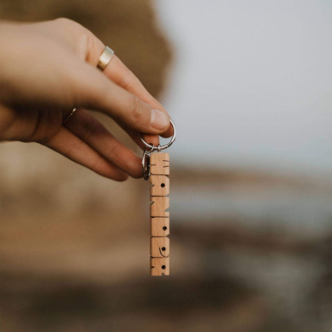 Hand holding Trek Light WANDER wood keychain with nickel ring, perfect gift idea. Elegant hand-cut design for keys.